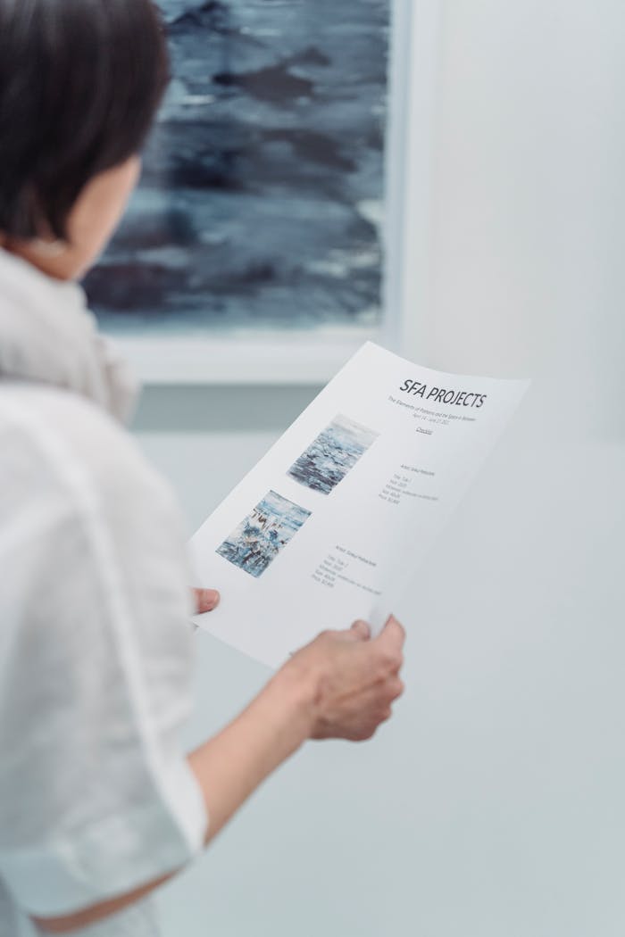 about-02 A woman examines an art project document at a gallery, focusing intently on the details.